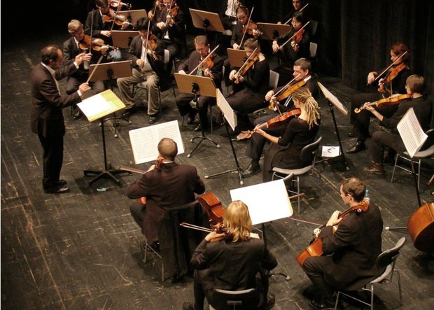 Orchester auf Bühne aus leichter Vogelperspektive mit Dirigenten