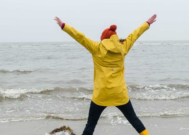 Frau springt in Regenjacke am regnerischen Meer