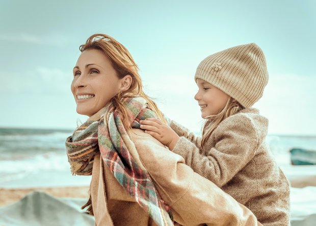 Mutter mit Kind auf dem Rücken am Meer