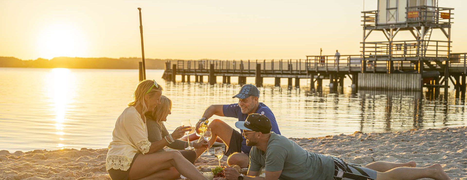 Gruppe mit Picknick am Strand vor der Seebrücke bei Sonnenuntergang