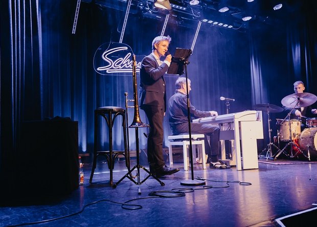 Musiker-Trio David, Ben und Finn auf der Bühne in blauem Licht mit Piano, Posaune und Schlagzeug, 