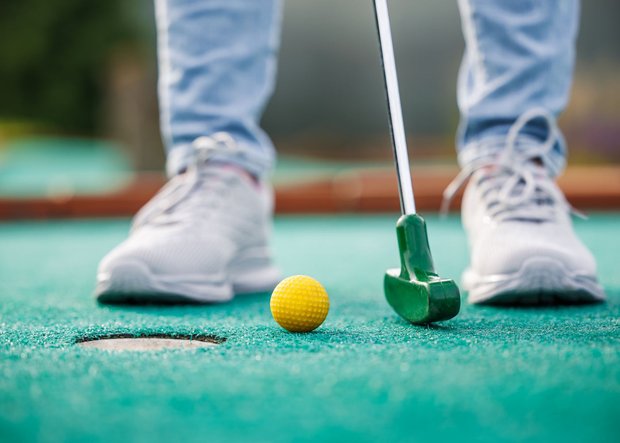 Minigolf Loch und Schläger mit Füßen in der Nahaufnahme
